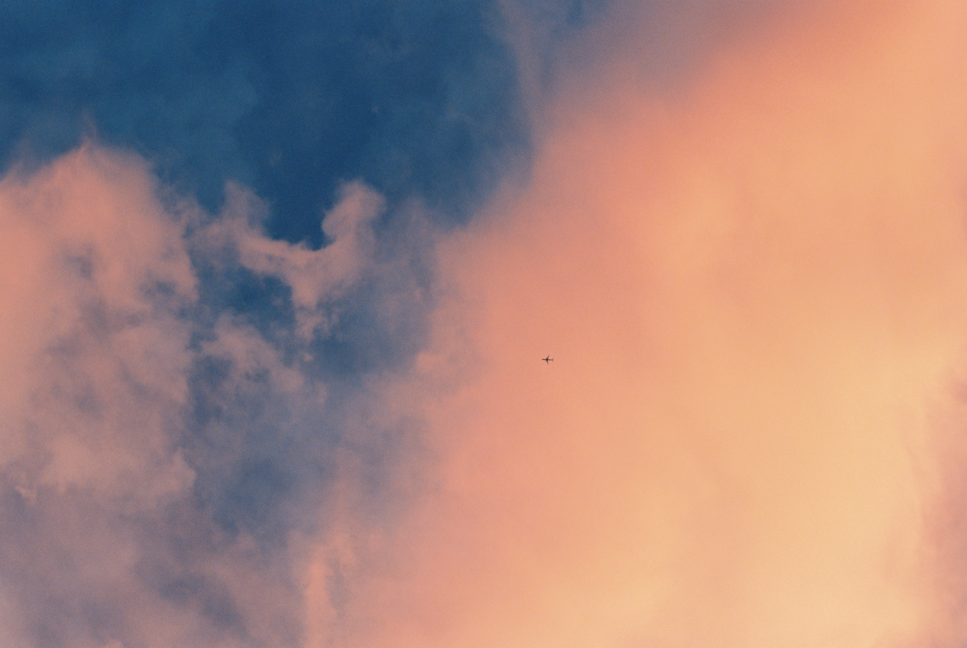 Color photo of a plane against clouds at sunset.